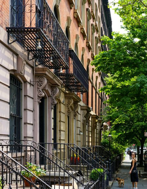 A row of iconic brownstones with wrought iron details on a sunny urban street.